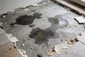 Estrichboden mit mehreren dunklen Feuchtigkeitsflecken und umgebrochenen Bodenplatten